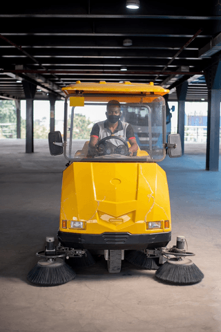 FixIt operator driving a ride-on sweeper in a covered terminal